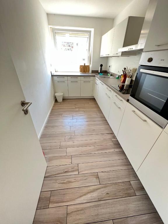 a kitchen with white cabinets and a wooden floor at Monteurwohnung Pforzheim mit Balkon - QuartierPro in Pforzheim