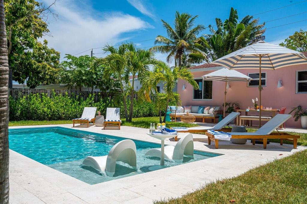 einem Pool mit Stühlen und einem Sonnenschirm neben einem Haus in der Unterkunft The Coral Cabana Modern Palm Beach Escape in West Palm Beach
