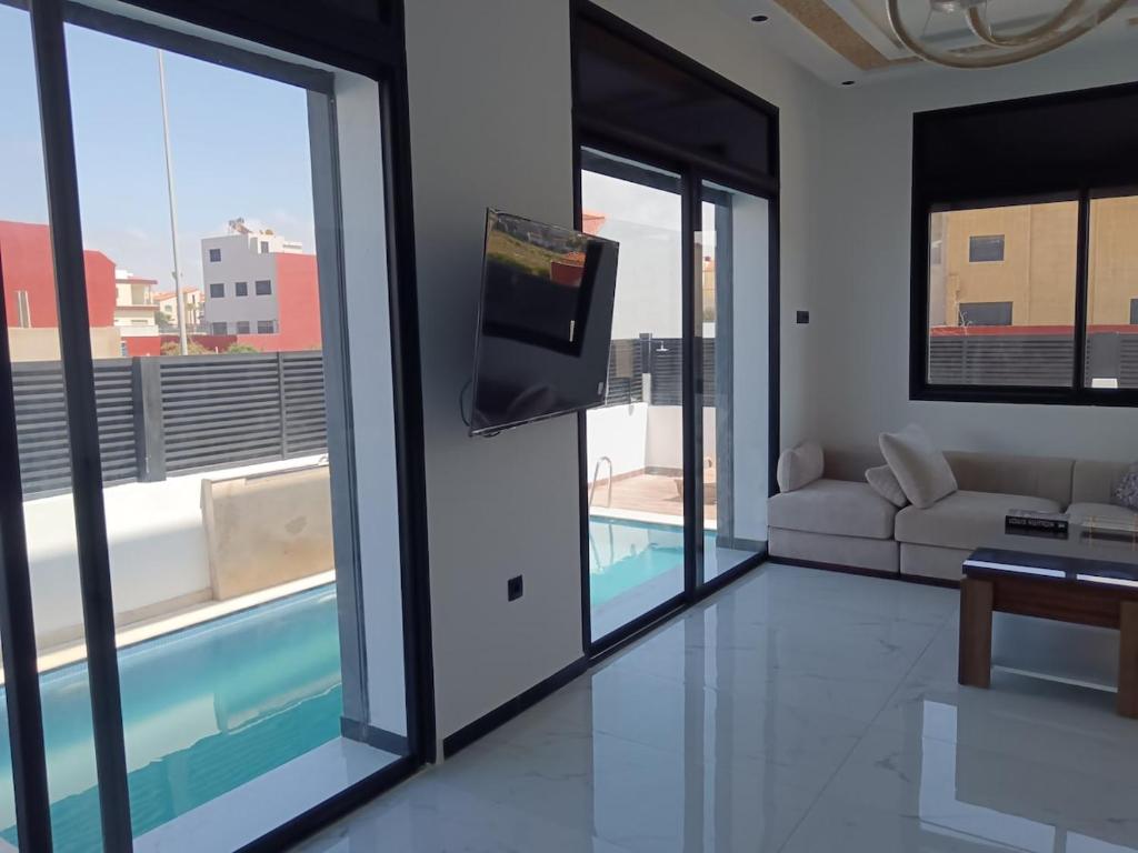 a living room with a couch and a tv and windows at Villa Chez Badre with Pool High Standing in Sidi Rahal