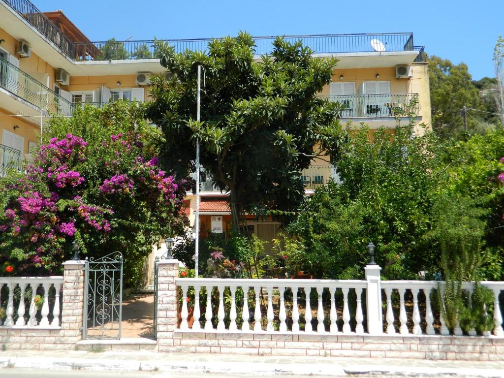 a white fence in front of a building with flowers at Logaras Apartments in Ayia Evfimia