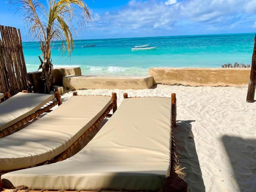 two beds on the beach with a boat in the water at Aquelia Rose Hotel in Jambiani
