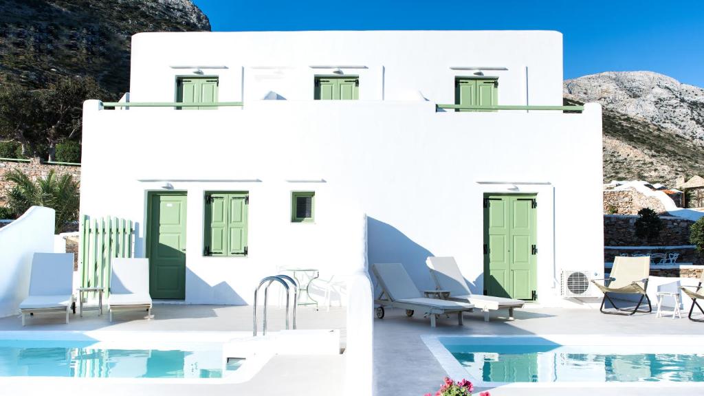 Casa blanca con puertas verdes y sillas junto a una piscina en Xerolithia Land, en Kamarai