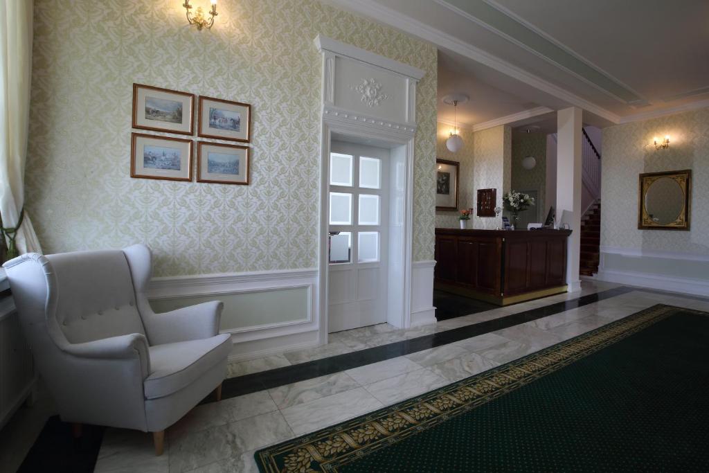 Classic hotel lobby with wingback armchair, patterned wallpaper, marble floor and wooden reception desk.
