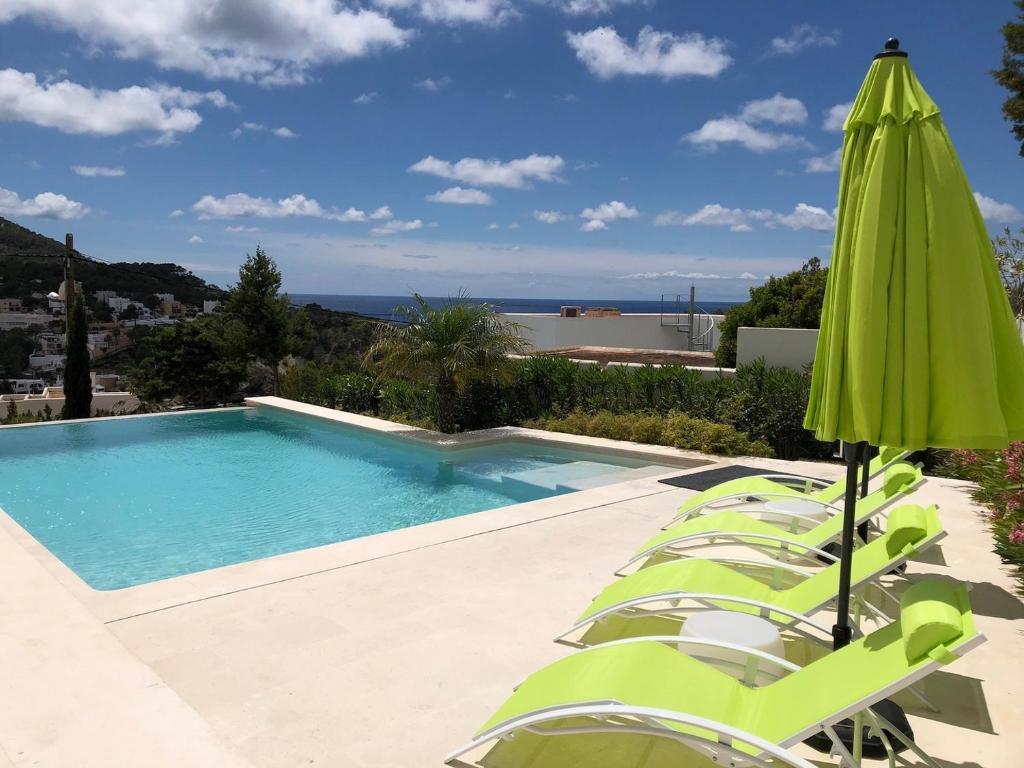 una piscina con sedie e ombrellone verde di Exclusive Villa Retreat in Ibiza City, 1075 a Cala Vadella