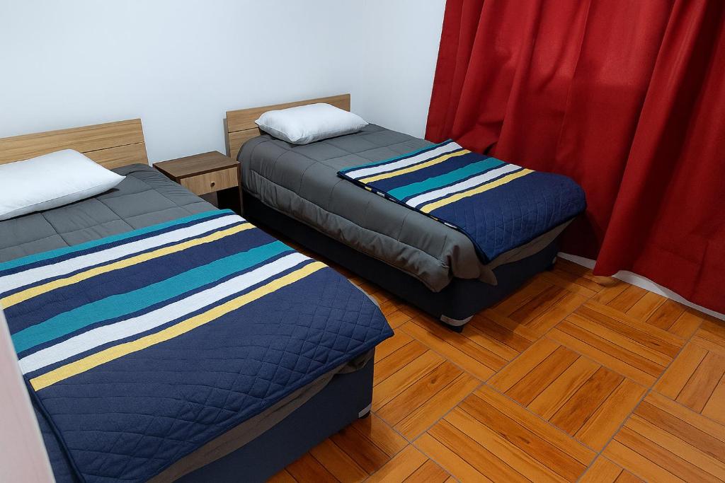 two beds in a room with red curtains and wooden floors at Parcela Santa Elena, Cabaña1 in San José de Maipo