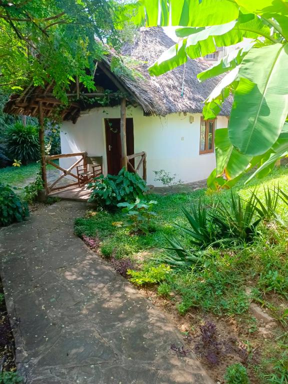 a house with a thatched roof and a path in front at The Makuti breeze house in Mtwapa