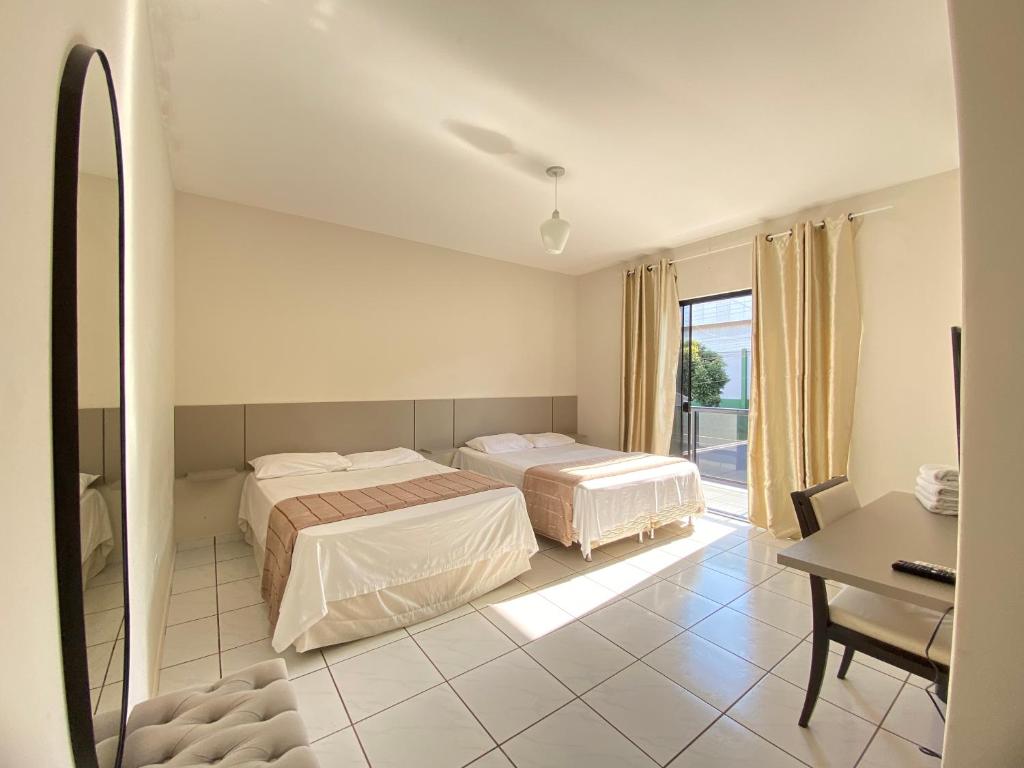 a bedroom with two beds and a table and a desk at Pousada DONA LÍDIA in Campo Mourão