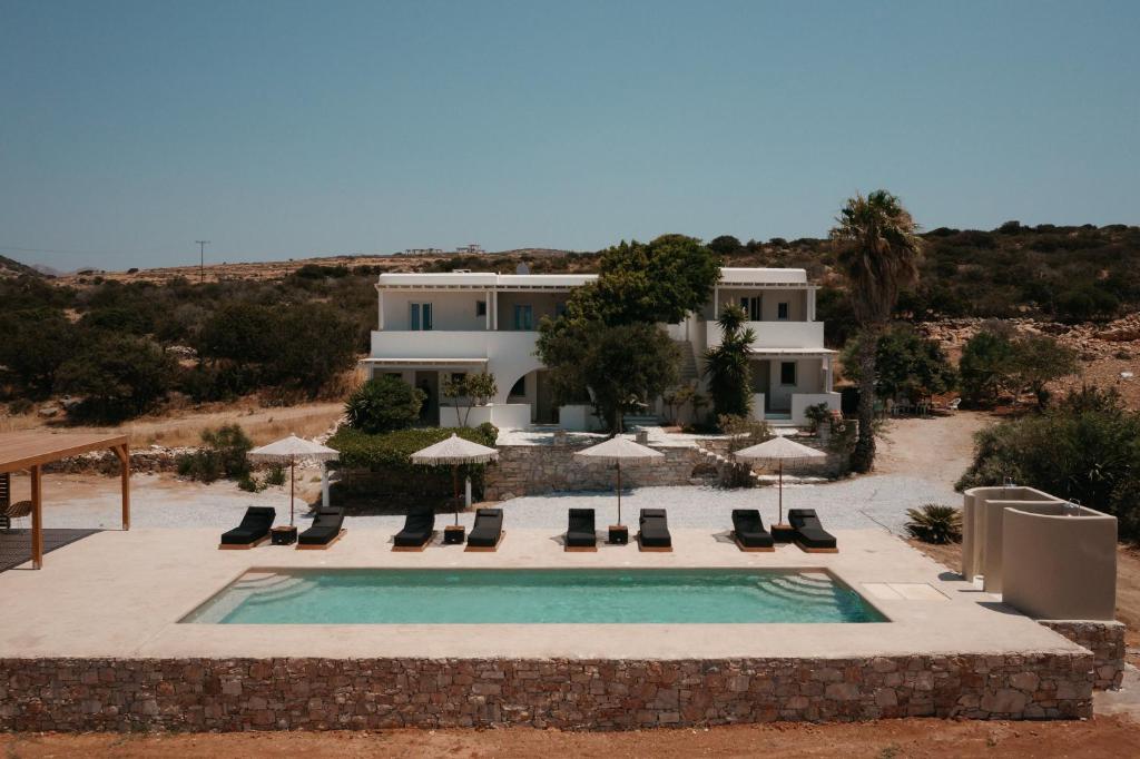 a pool with chairs and umbrellas in front of a house at Phoenicia Nature Naxos in Kastraki