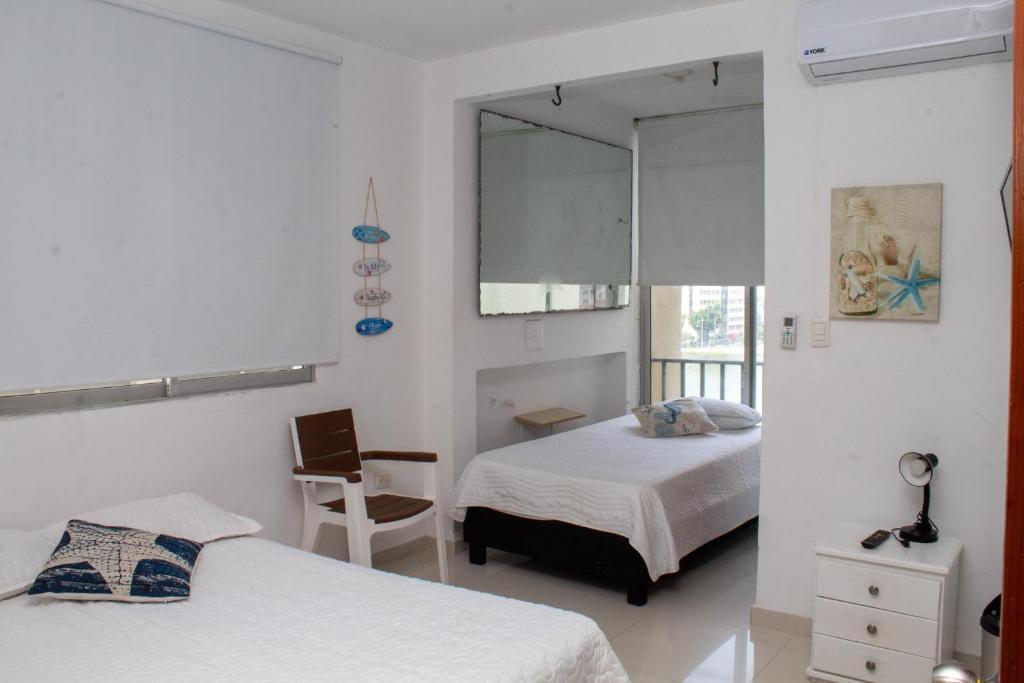 ein weißes Schlafzimmer mit zwei Betten und einem Spiegel in der Unterkunft Encantador Apartamento El Laguito Bocagrande in Cartagena de Indias