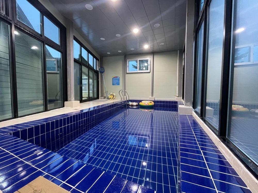 a swimming pool with blue tiles in a room with windows at Daebudo Nurimaru Pension in Ansan