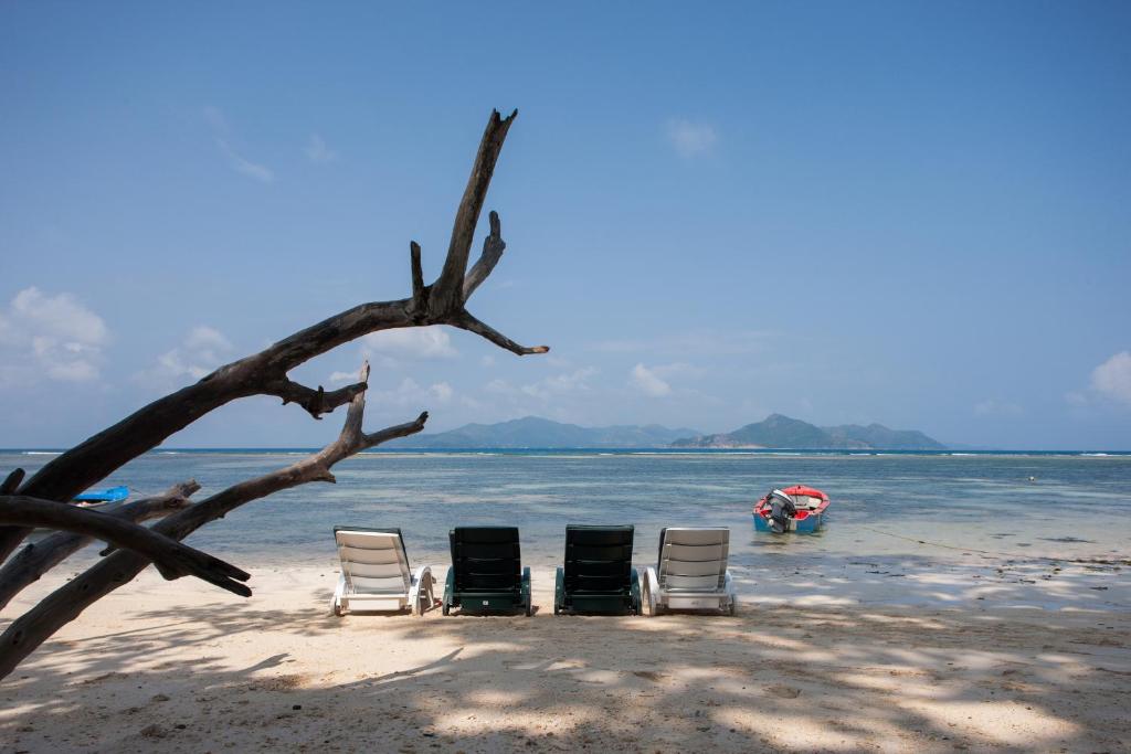 three chairs and a tree on a beach with a boat at Le Relax Self Catering Apartment in La Digue