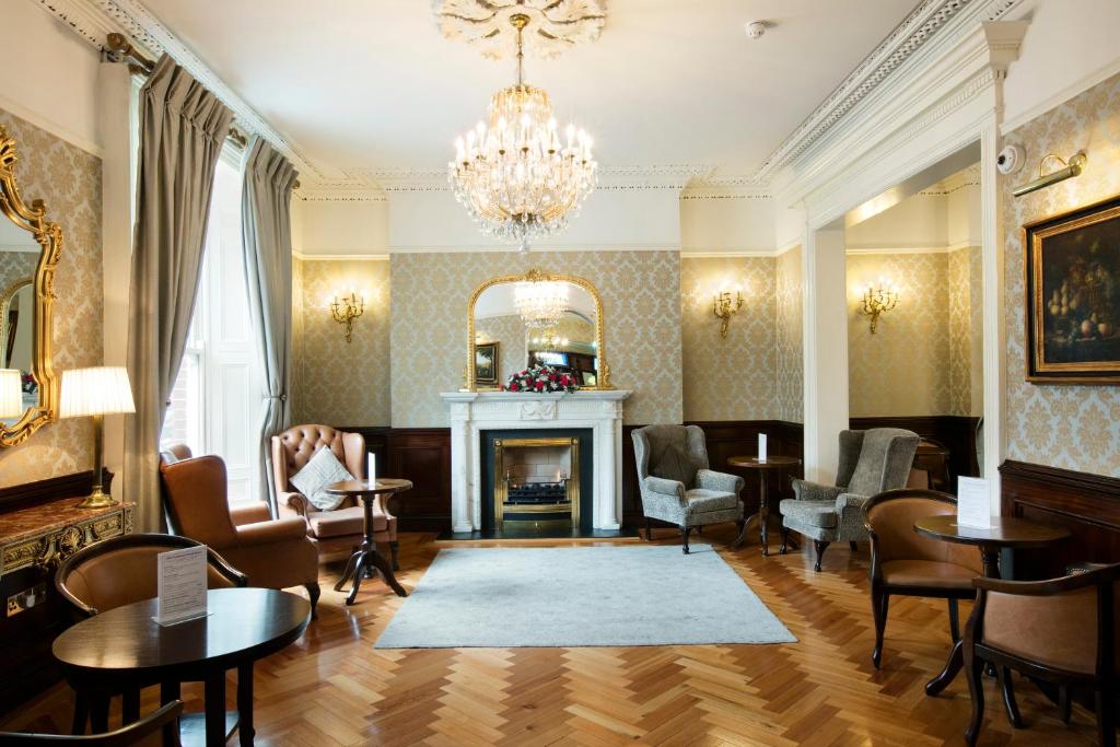 a living room with a fireplace and chairs and a chandelier at Harcourt Hotel in Dublin