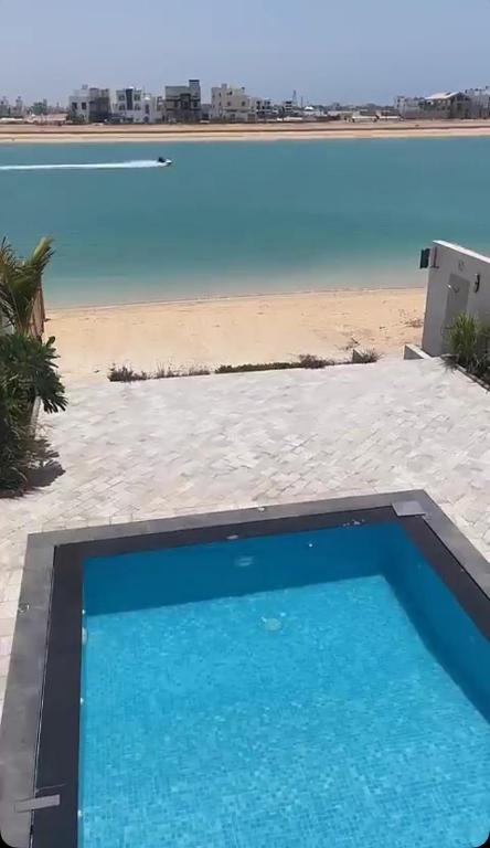 a blue swimming pool next to a beach at Soso beach villa in Durat Alarous