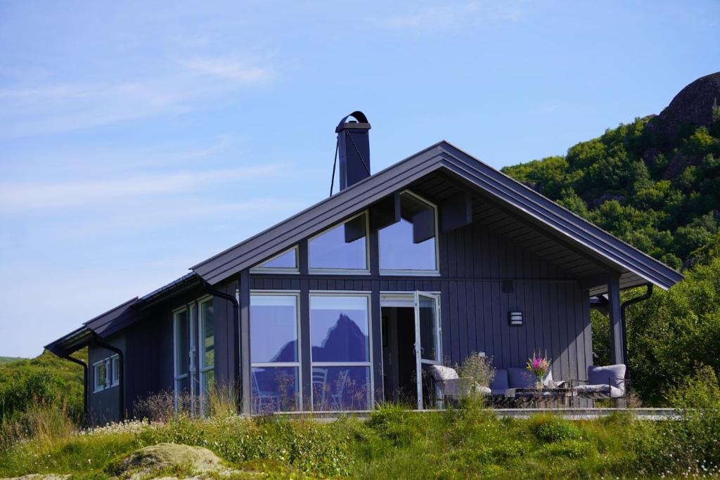 a black cottage with large windows and mountains in the background at Sea Pearl Lodge in Leknes