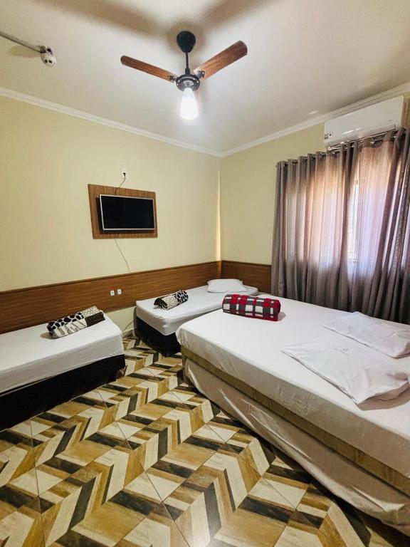 two beds in a room with a ceiling fan at Pousada Mãe Padroeira in Aparecida