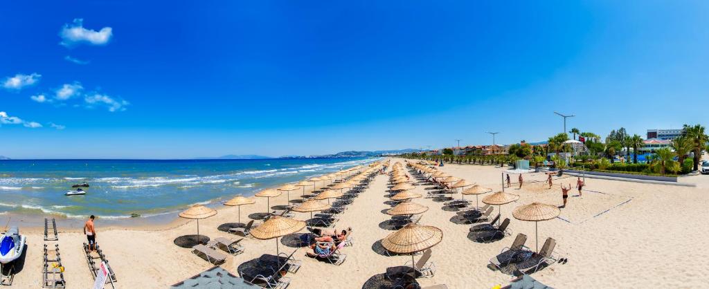 a beach with chairs and umbrellas and the ocean at Flora Garden Ephesus Kusadasi - All Inclusive in Davutlar
