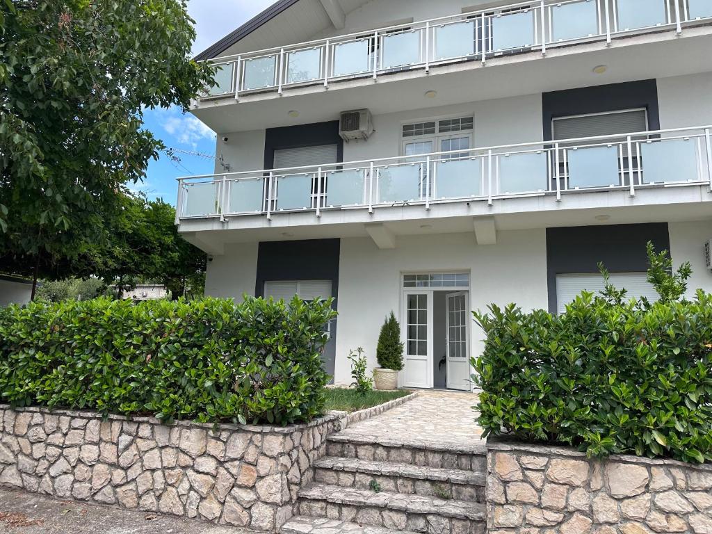 a white house with a balcony and bushes at Apartmani Novak in Mostar