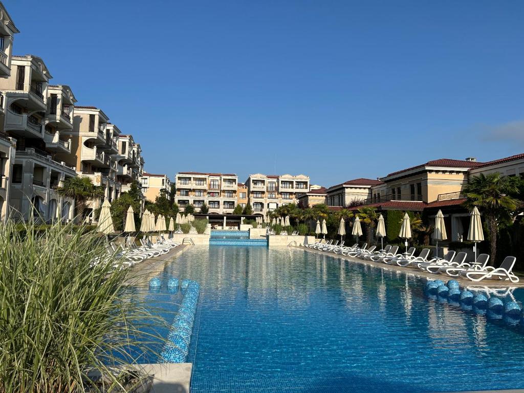 a swimming pool with chairs and umbrellas and buildings at Студио Premium,Смокиня,Созопол,5звезден затворен комплекс,4 басейна,1ва линия море 