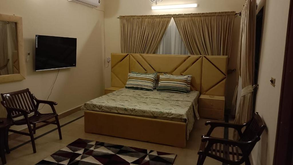 een slaapkamer met een bed met 2 stoelen en een televisie bij Royal one cottage in Islamabad