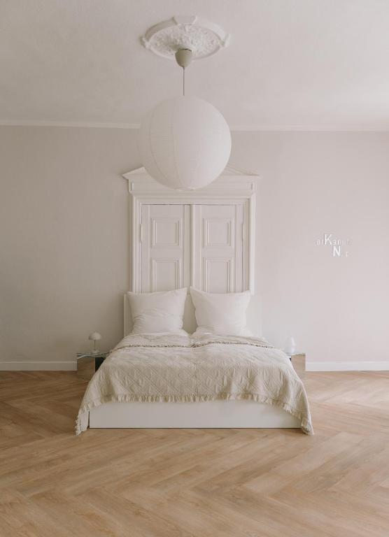 a white bedroom with a bed and a chandelier at Arkanum Studio in Altenburg