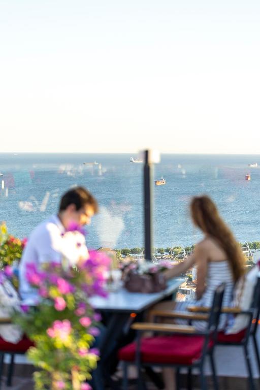 a man and woman sitting at a table with the ocean in the background at Olimpic Hotel in Istanbul