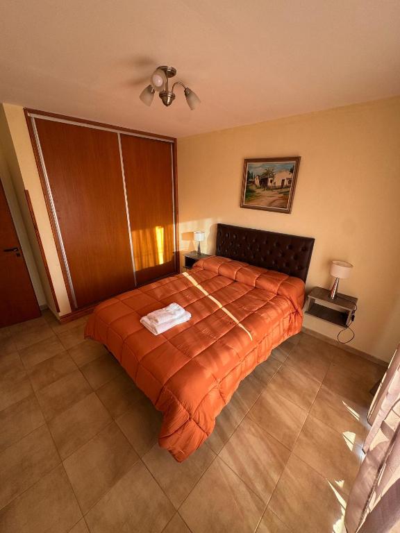 a bedroom with a large bed with an orange blanket at Apart Dinkendein de 2 dormitorios in Río Cuarto
