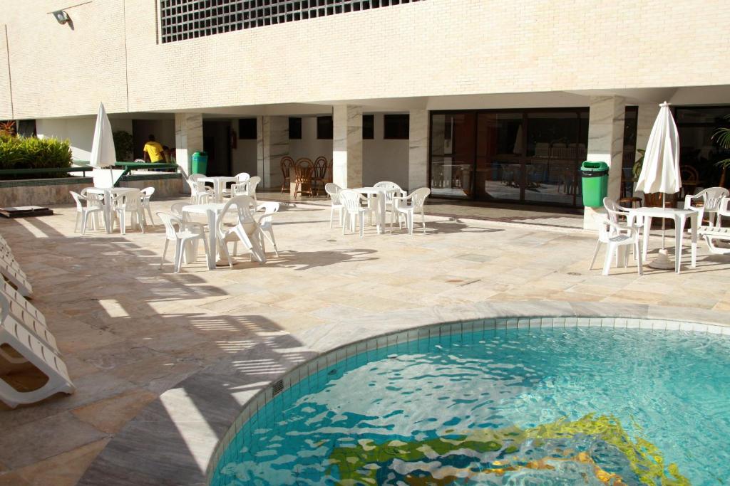 una piscina con sedie e tavoli bianchi e un edificio di Apart Hotel Atlantic City Salvador a Salvador