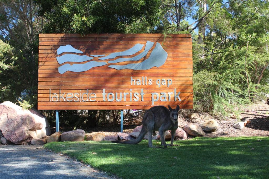 un perro parado frente a un cartel en Halls Gap Lakeside Tourist Park en Halls Gap