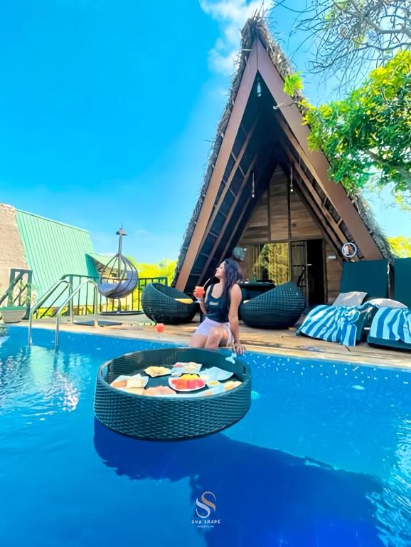 a woman sitting on the edge of a swimming pool in front of a house at Private Pool Sun Shade Resort & Spa in Habarana