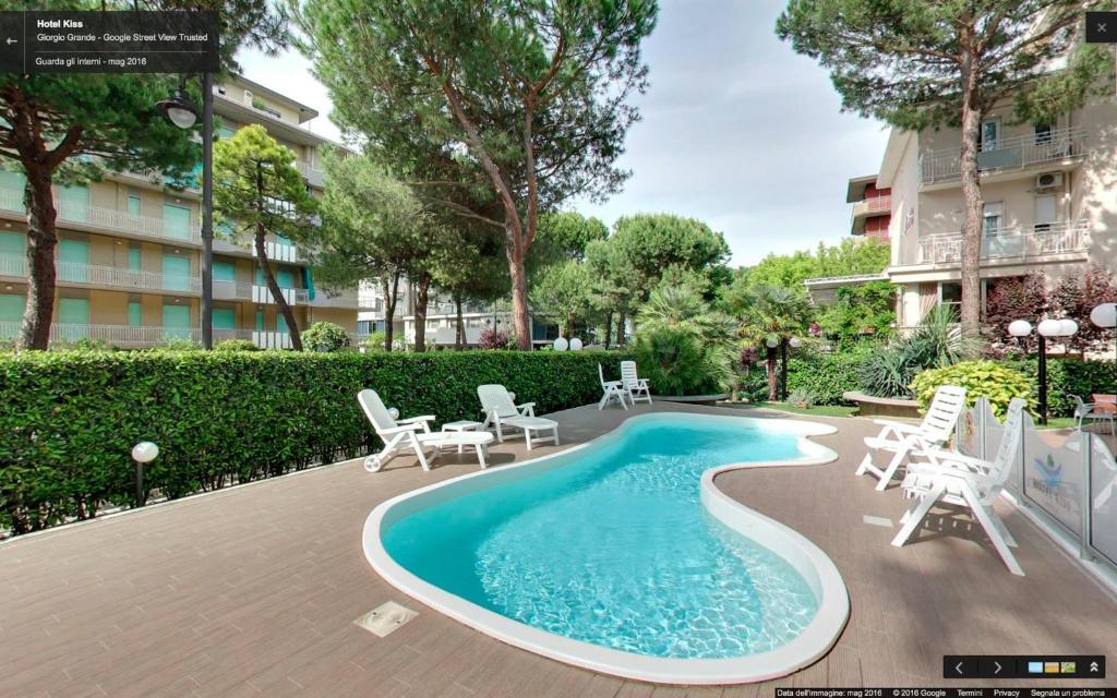 a swimming pool with chairs and a table and a building at Hotel Kiss in Cesenatico