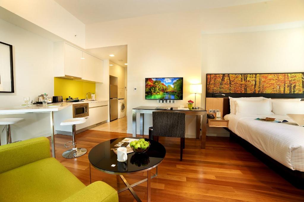 An open-plan serviced suite combining a bed, kitchenette, dining counter, desk and lounge chair.