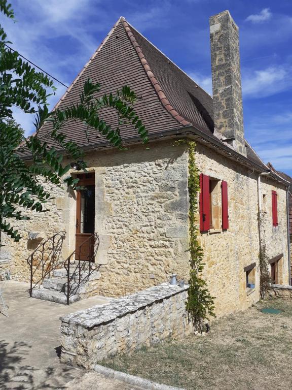 an old stone house with a chimney and red shutters at Maison périgourdine proche de Sarlat in Daglan
