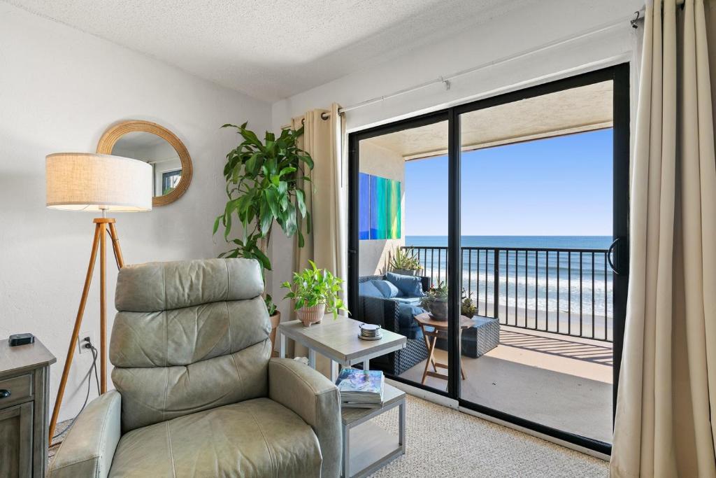 a living room with a chair and a balcony with the ocean at 512 - Oceanfront top floor corner 2 bedroom in New Smyrna Beach