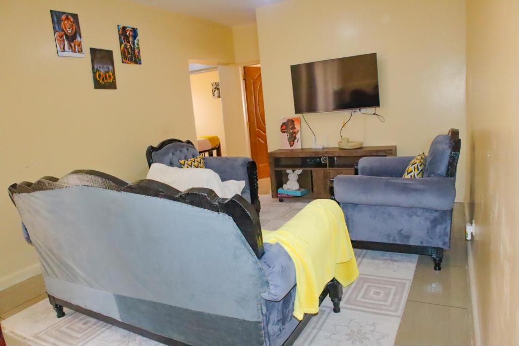 een woonkamer met twee blauwe stoelen en een flatscreen-tv bij Kings Square Tebiz Haven in Eldoret