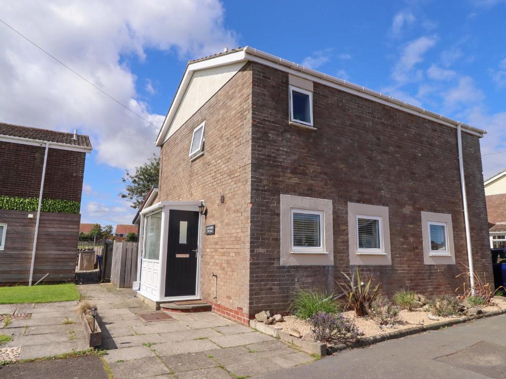 a brick house with a white door on a street at Lavender Cottage in Chathill