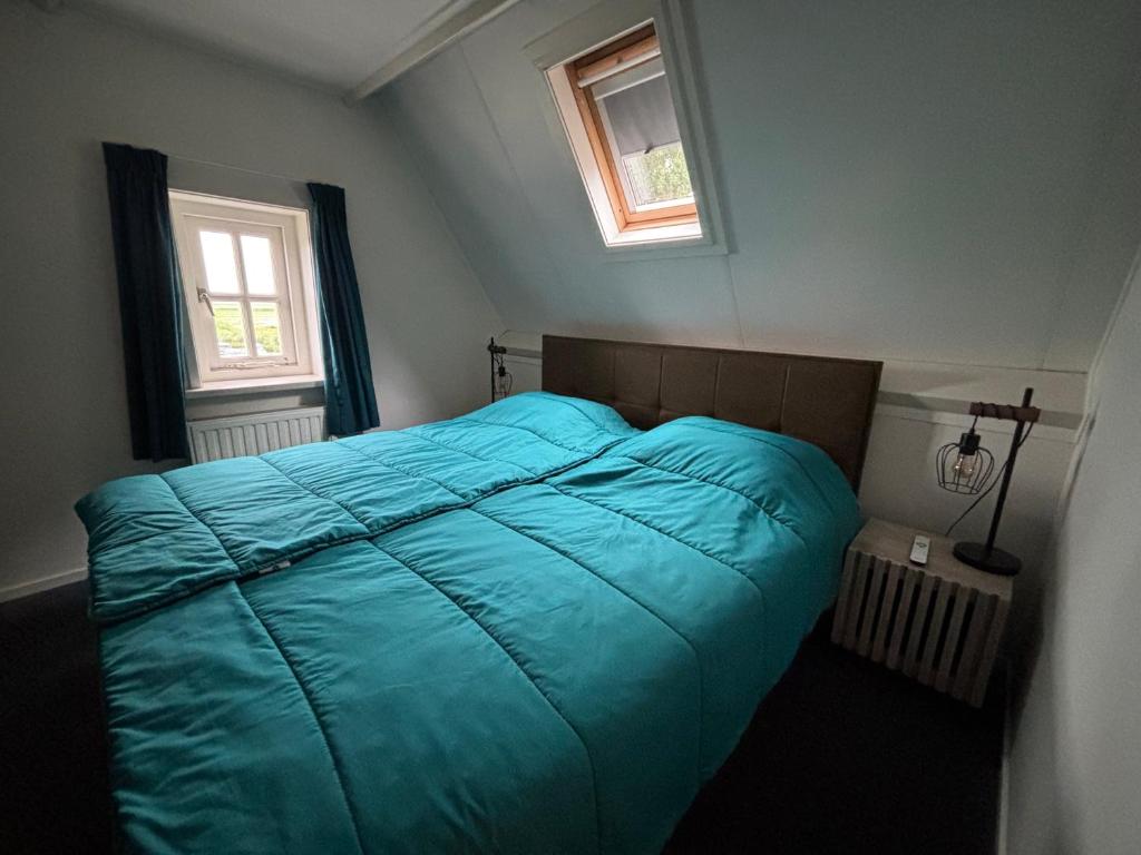 een slaapkamer met een blauw bed en 2 ramen bij Ut ânker fan de Jong in Hollum