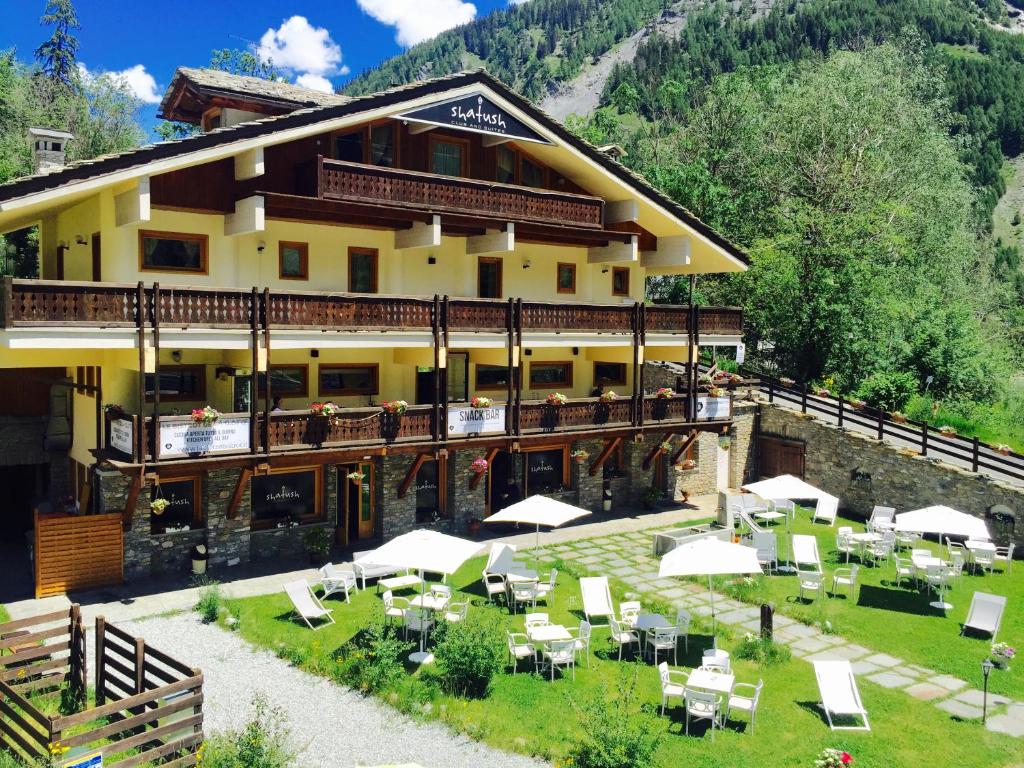 un grand bâtiment avec des tables et des chaises devant lui dans l'établissement Shatush Hotel, à Courmayeur