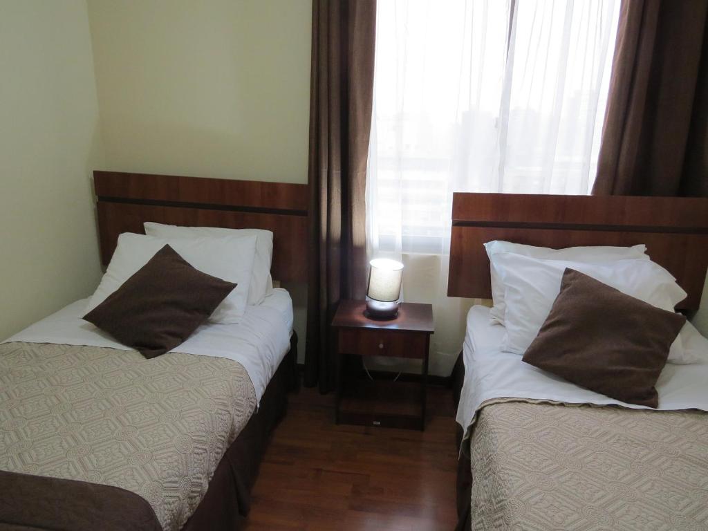 two beds in a hotel room with a window at Apartments Bellas Artes in Santiago