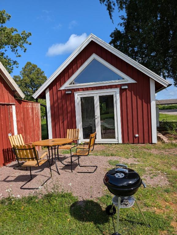 a picnic table and chairs and a grill in front of a red barn at Kleines modernes Haus in Borghamn in Borghamn