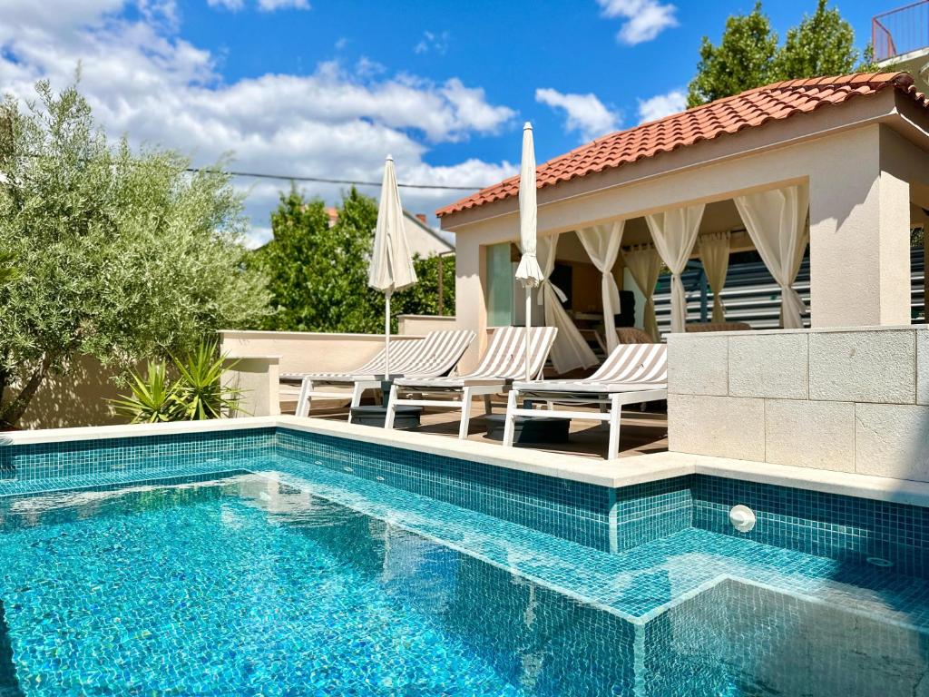 a swimming pool with chairs and a house at Apartments Villa A - Heating Pool in Trogir