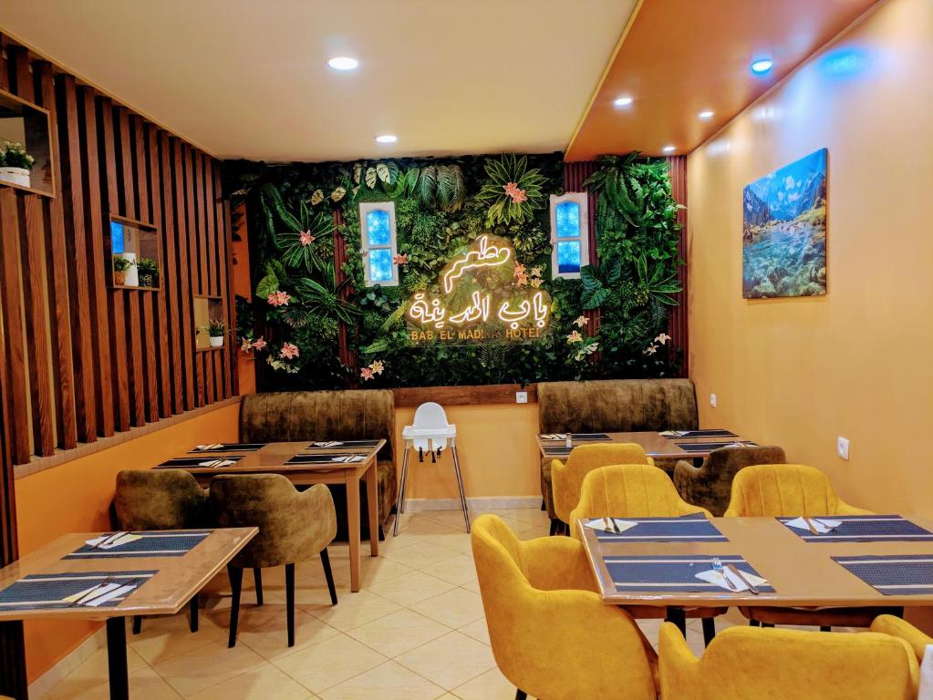 un restaurante con mesas y sillas y una pared con plantas en HOTEL Bab El Madina, en Adrar