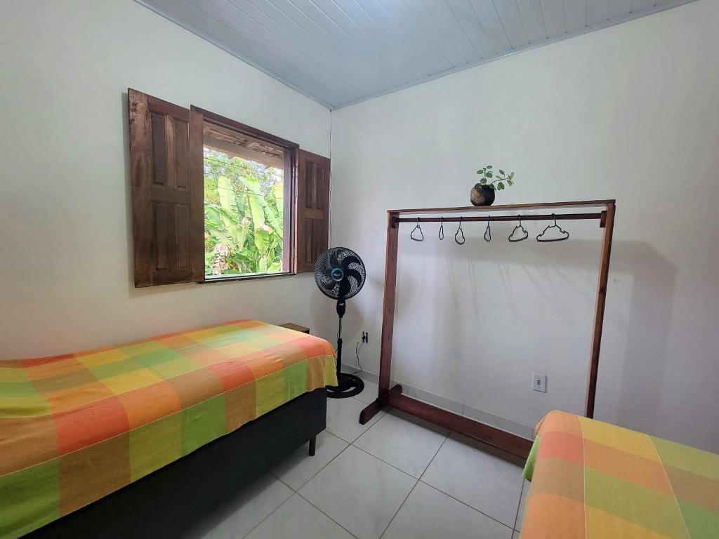 a bedroom with two beds and a window and a fan at Quarto Compartilhado na Praça de Serra Grande in Uruçuca