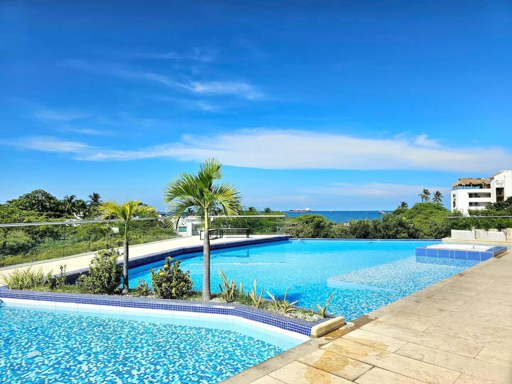 ein Swimmingpool mit Palmen und dem Meer in der Unterkunft Apto de Ensueño Frente al Mar in Playa Bello Horizonte