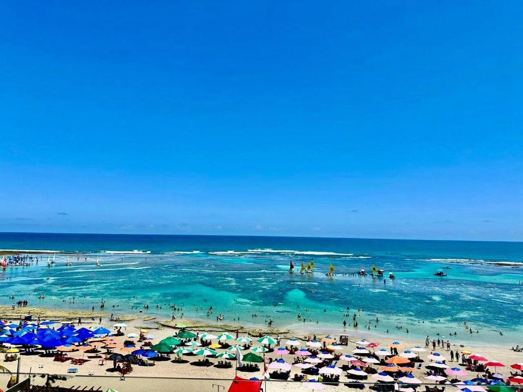 einen Strand mit Menschen im Wasser und Sonnenschirmen in der Unterkunft Mirante Porto Galinhas beira-mar in Porto De Galinhas