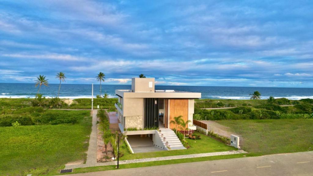 ein Haus am Strand mit dem Ozean im Hintergrund in der Unterkunft Mansão Pé na Areia 8 Suítes Alphaville Guarajuba in Barra de Jacuípe
