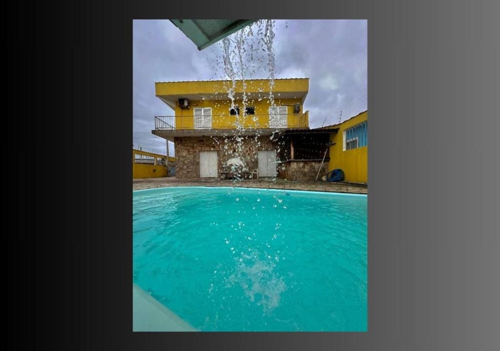 a swimming pool with a fountain in front of a house at Pousada Encanto in Mongaguá
