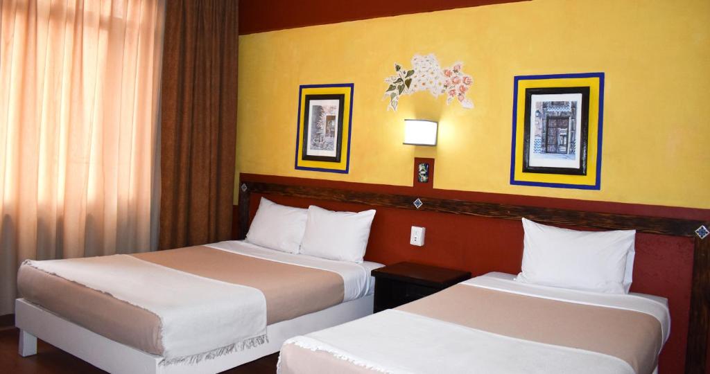 two beds in a hotel room with yellow walls at Hotel Benedicta in Mexico City