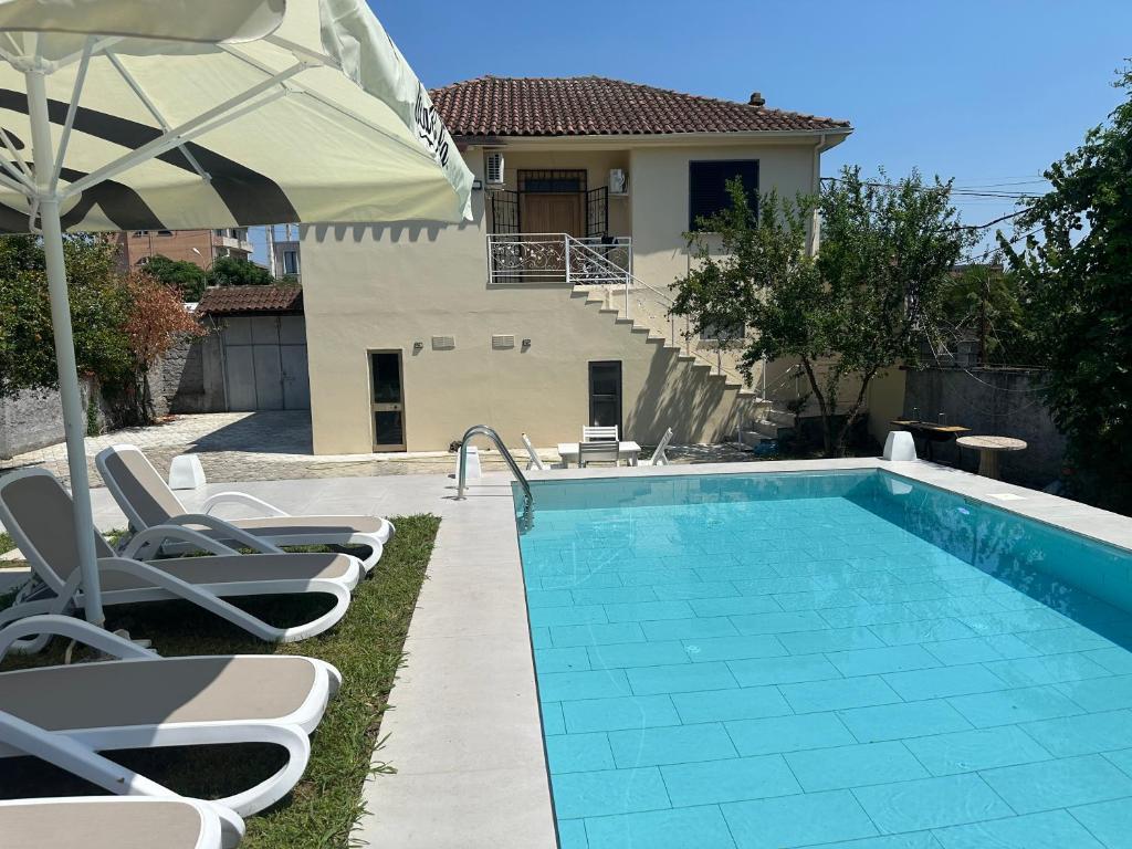 a swimming pool with chairs and an umbrella next to a house at La Piscina in Shkodër
