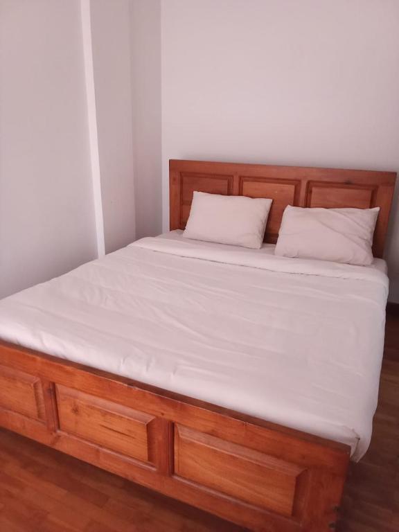 a bed with a wooden frame and white sheets at Glenfalls Residencies in Nuwara Eliya