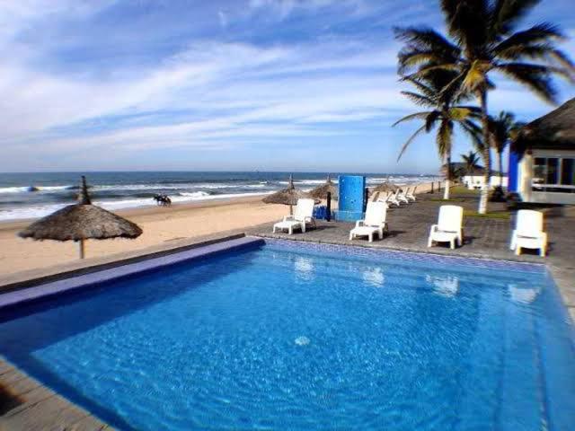 a swimming pool next to a beach with chairs and umbrellas at Casa de playa, a pasos del mar in Mazatlán